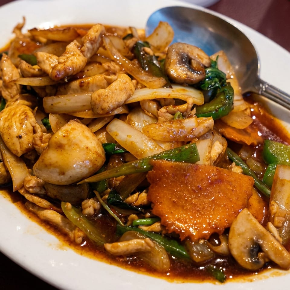 Stir-fried chicken with mushrooms, onions, peppers, and vegetables in a rich brown sauce on a white plate.