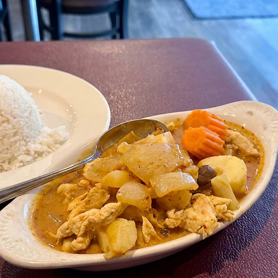 Plate of chicken curry with potatoes and carrots served alongside a mound of white rice on a restaurant table.